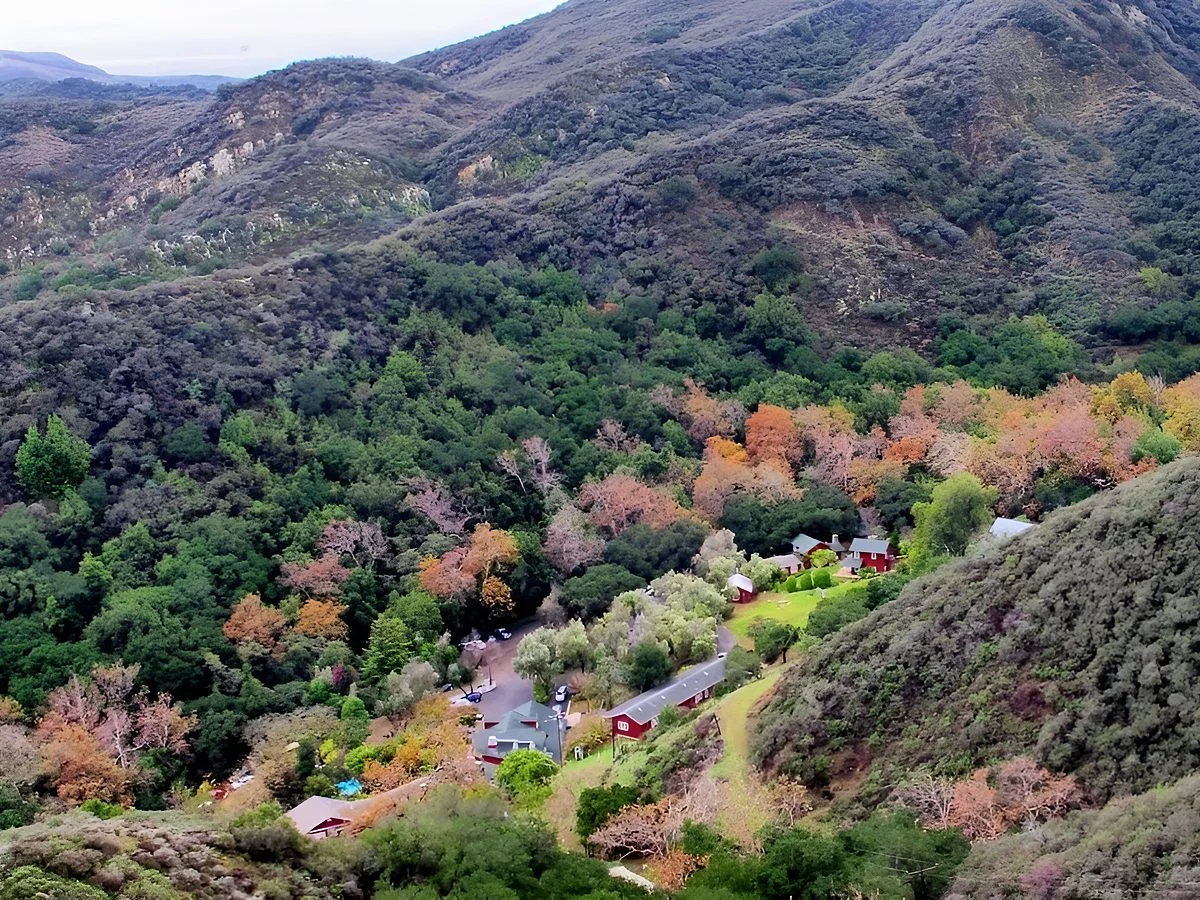 Looking down into the green canyon, the ranch buildings among the trees below the slopes