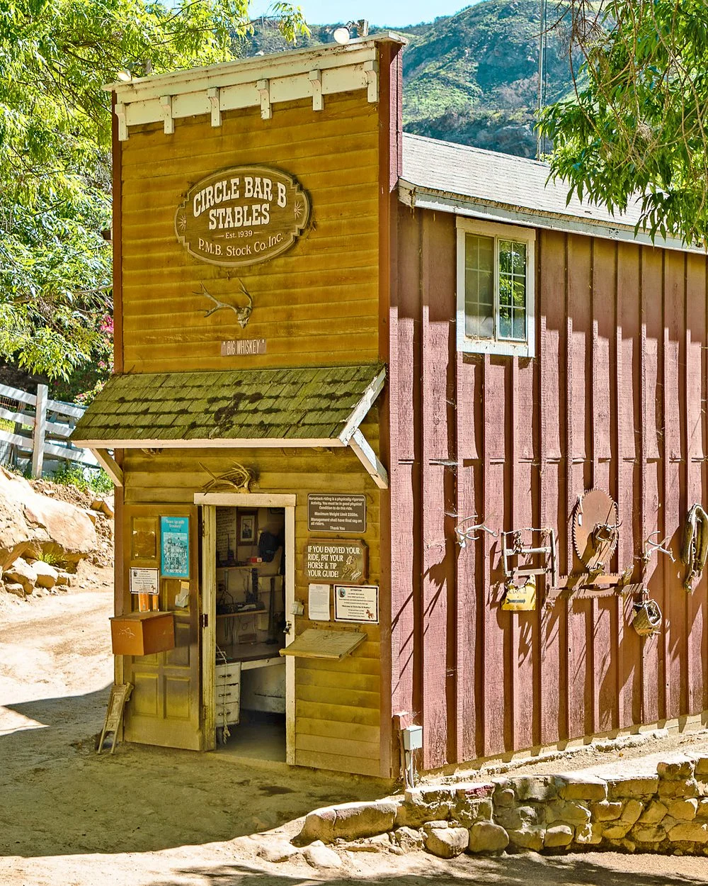The red false-front stables office in the shade of the trees, its oval sign reading Circle Bar B Stables