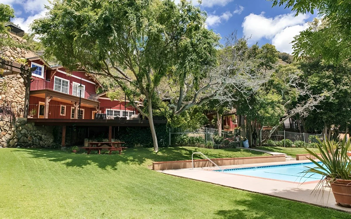 The red lodge on its stone base above the lawn, the pool in the foreground under the trees